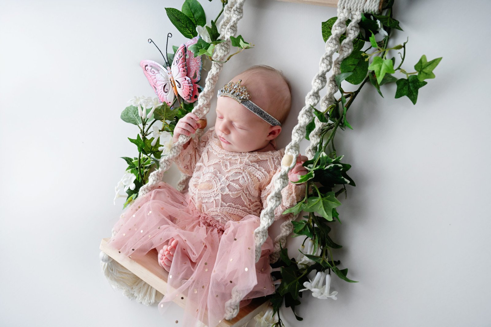 Newborn girl wearing pink and a princess crown sitting in a swing