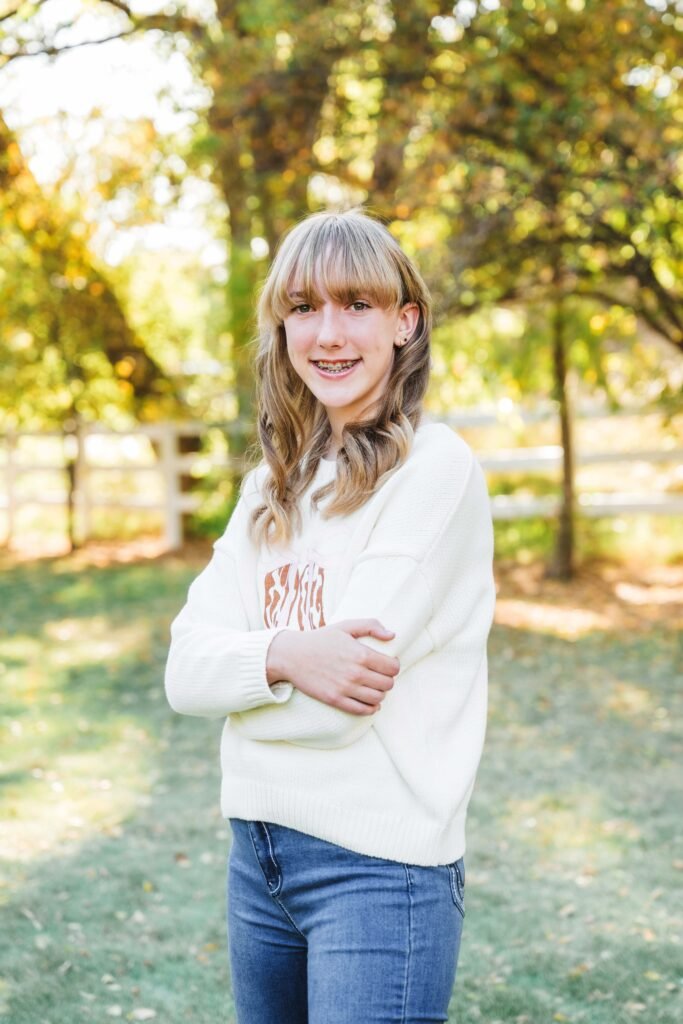 teenage girl posing for picture, arms folded, cream sweatshirt, jeans