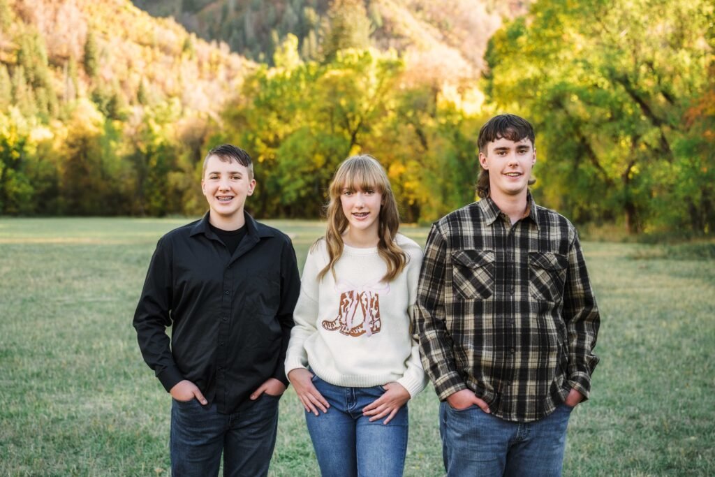 two teenage boys, one teenage girl in an open grassy field for a picture, mountains behind them