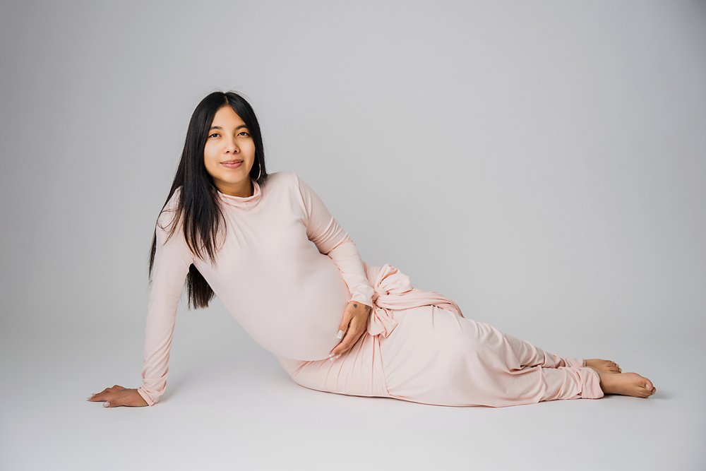 Utah Maternity Photography-pregnant woman in a long light pink dress sitting down with legs swept to the side